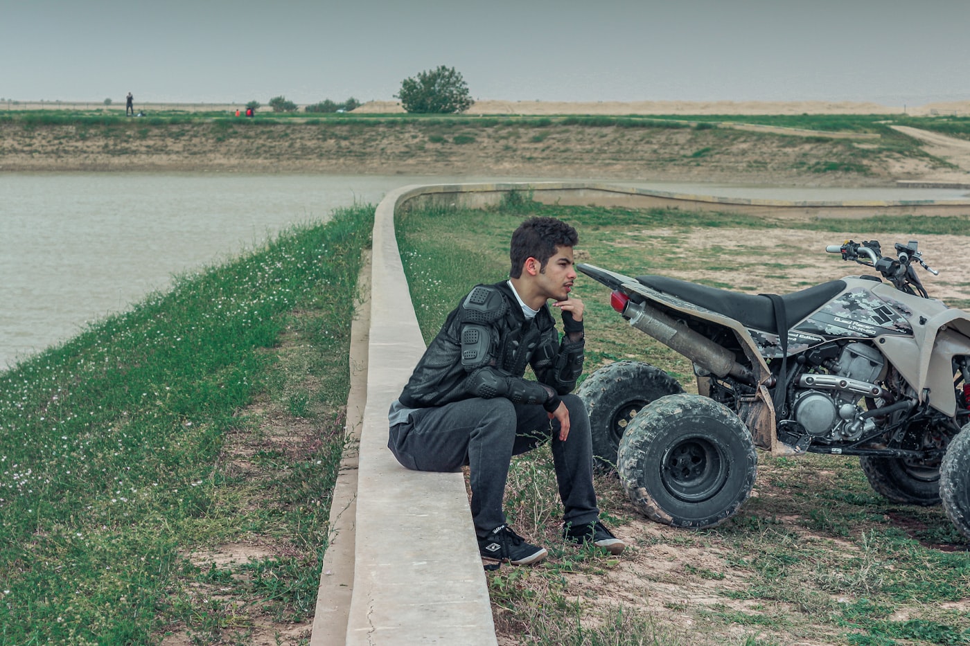 Person resting next to a quad ATV by a waterway on open terrain.