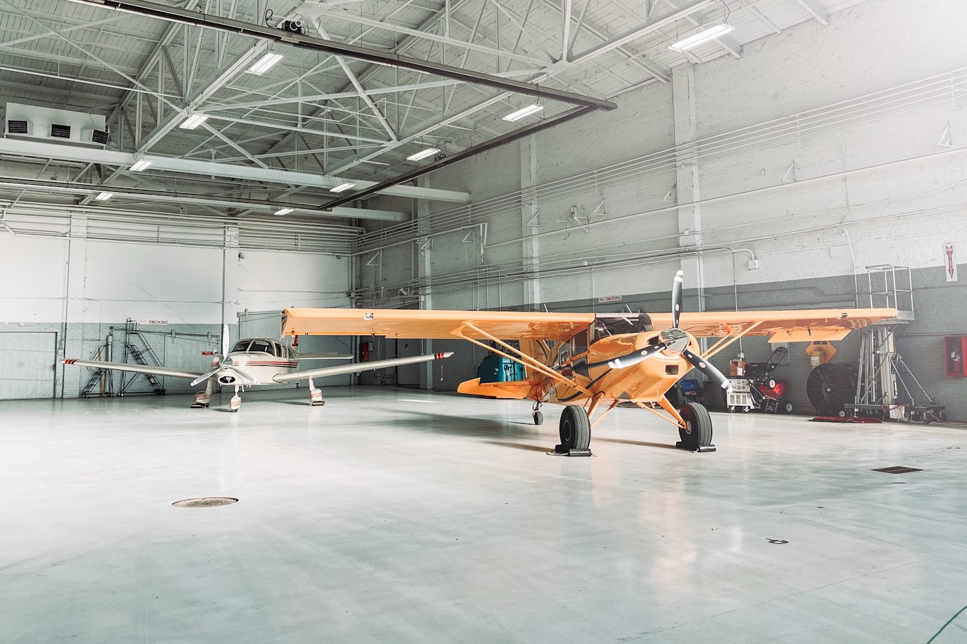Small orange airplane parked inside a clean aviation hangar.