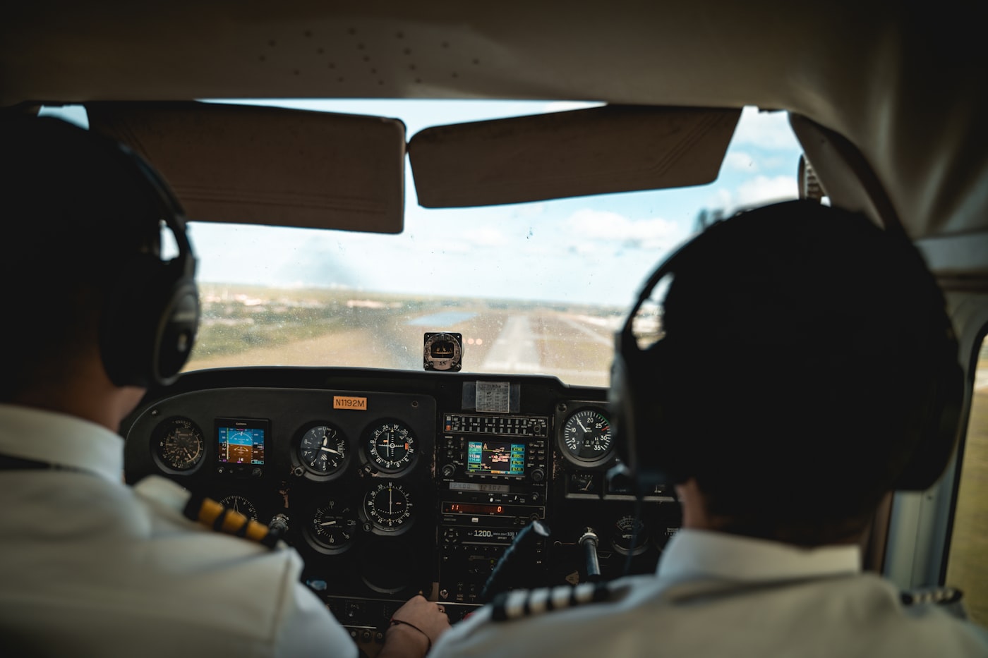 Two pilots in the cockpit of a small aircraft on approach to a runway.