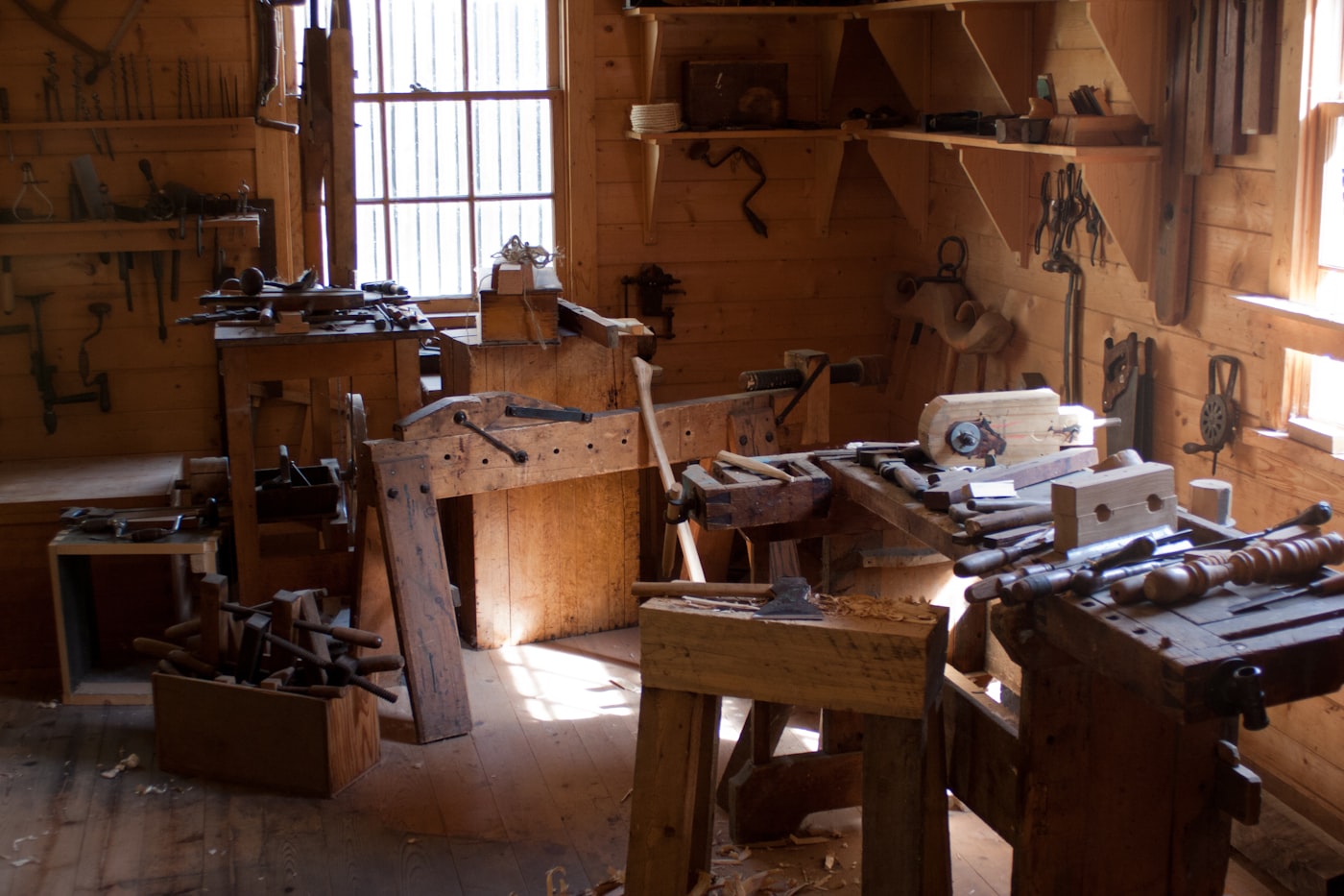 Sunlit traditional woodworking workshop filled with hand tools and workbenches.